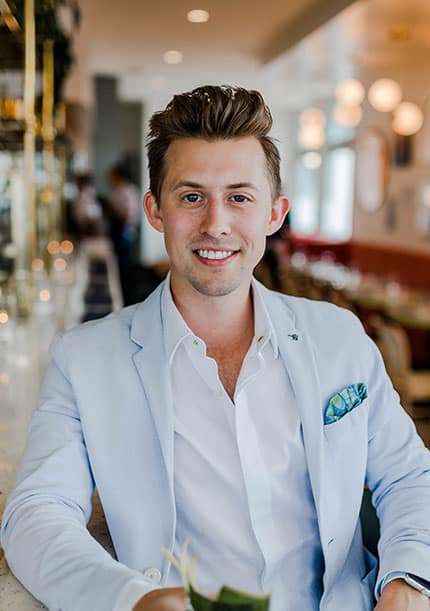 Young professional man in a light blue blazer smiling at a modern café.
